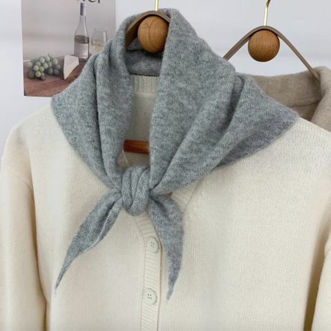 Pale grey skinny triangle wool scarf tied around a mannequin wearing a beige sweater with a blurred background