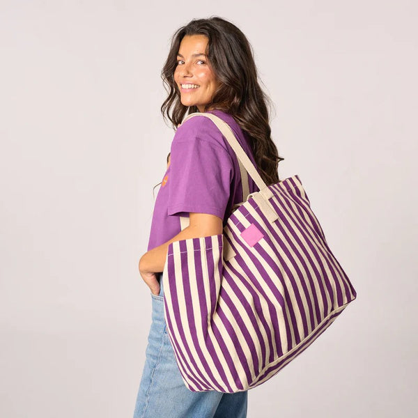 Woman carrying a purple and white striped tote bag on a plain background