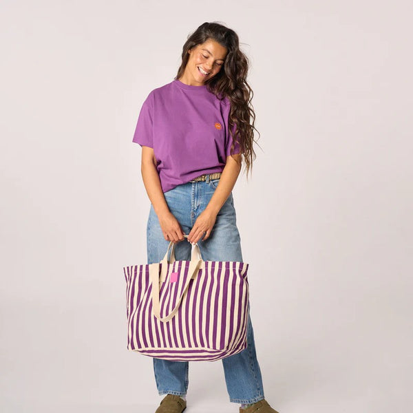 Woman holding a striped tote bag against a plain background