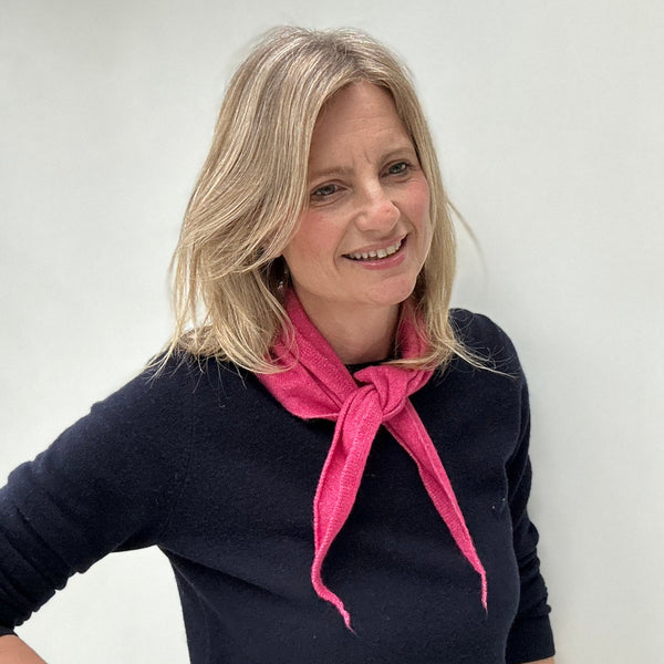 woman with blonde hair and a navy sweater wearing a raspberry pink wool triangle scarf