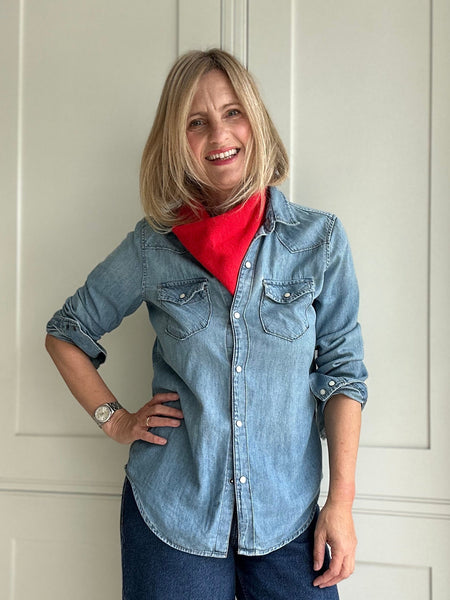 Woman wearing a denim shirt and jeans standing in front of a white door.