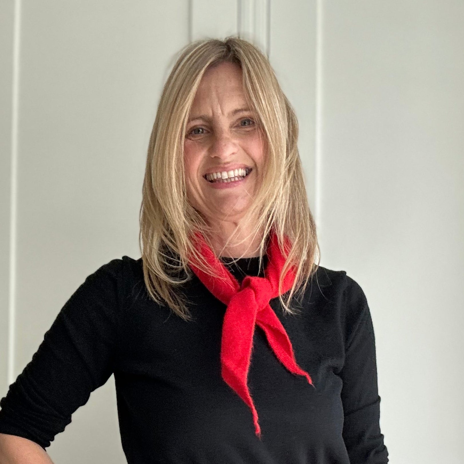 Woman wearing a black dress with a red scarf standing indoors.