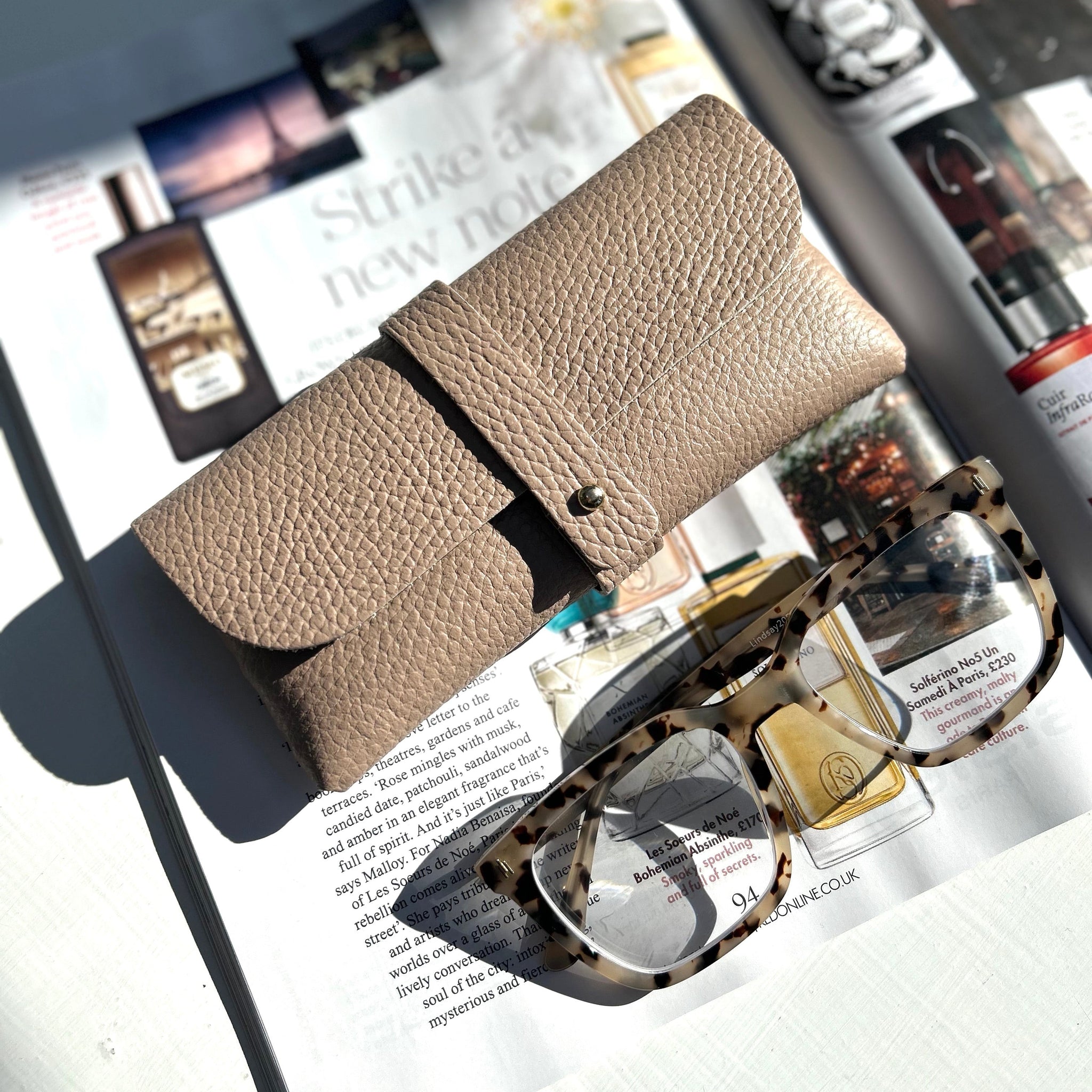 rose pink leather glasses case on top of a magazine with a pair of tortoiseshell glasses