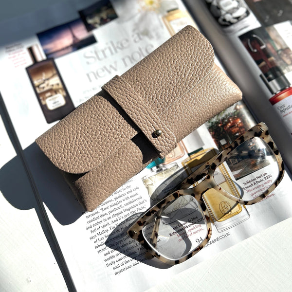 rose pink leather glasses case on top of a magazine with a pair of tortoiseshell glasses