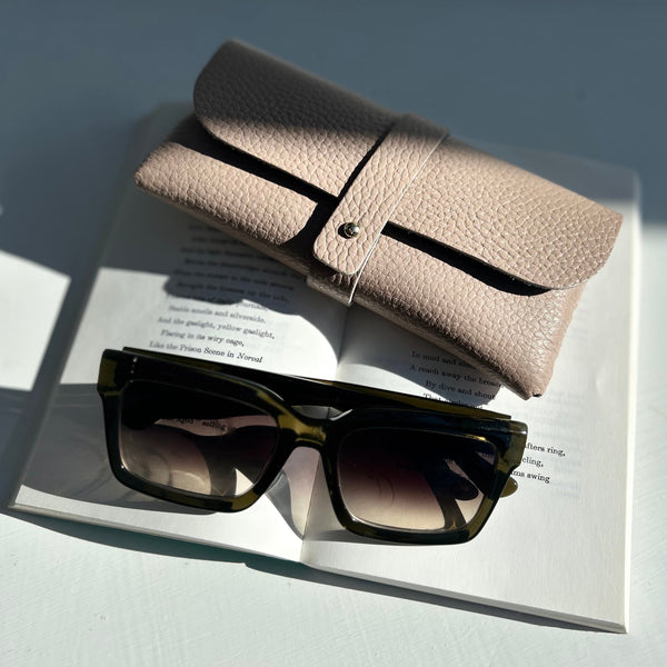 rose pink leather glasses case on top of a poetry book with a pair of green sunglasses
