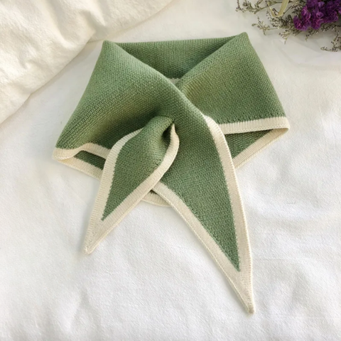 Green and white knitted triangle scarf  on a white surface with purple flowers in the background