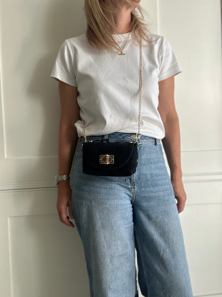 Person wearing a white t-shirt and blue jeans, holding a black handbag against a neutral background