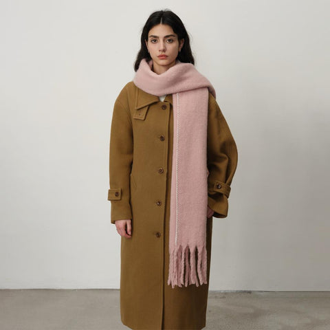 woman in camel coat with soft pink blanket scarf against a white background.