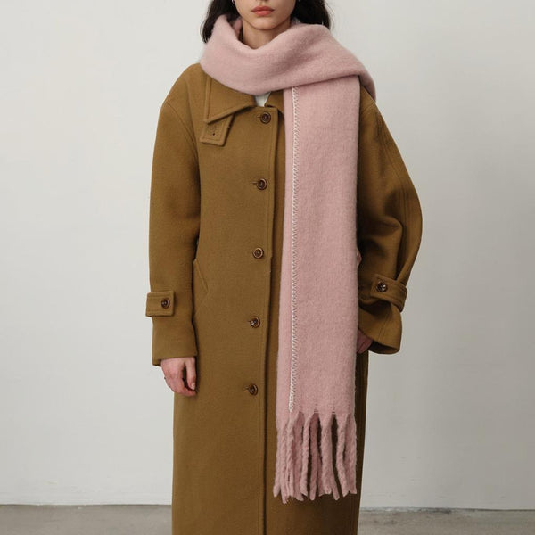 woman in camel coat with soft pink blanket scarf against a white background.