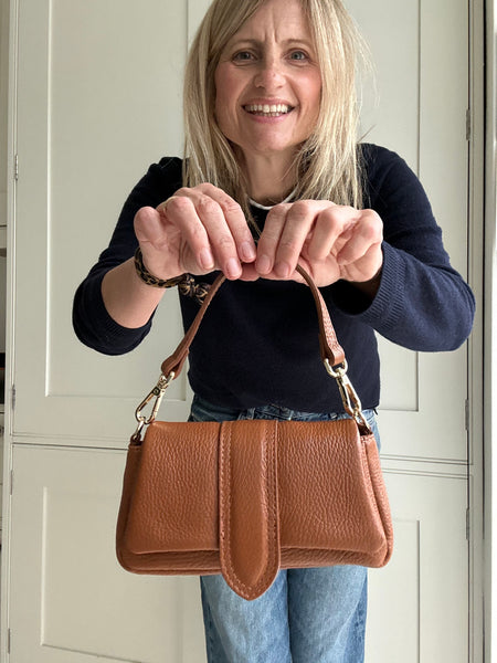 Woman holding a tan brown leather handbag in front of a white door