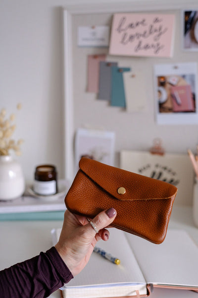 Person holding a tan leather purse in a room with decor elements.