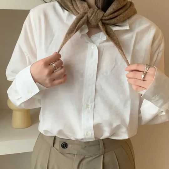 Woman wearing a white shirt with a taupe skinny triangle knit wool scarf around her neck, holding it with both hands.