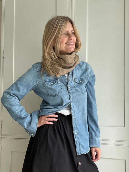 Woman wearing a denim jacket and black skirt indoors with a taupe wool scarf