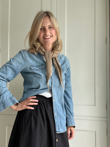 Woman wearing a denim jacket and black skirt indoors with a taupe wool scarf