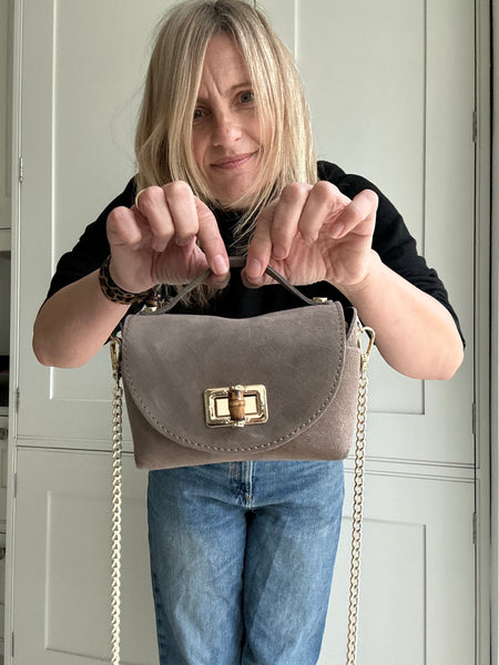 Person holding a taupe handbag with a chain strap in front of a white door.