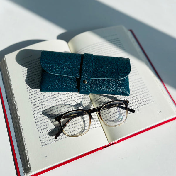 Teal Leather Glasses Case with ace and tate glasses on a book