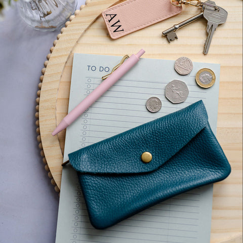 Teal Blue leather wallet with coins, pen, and keys on a wooden surface